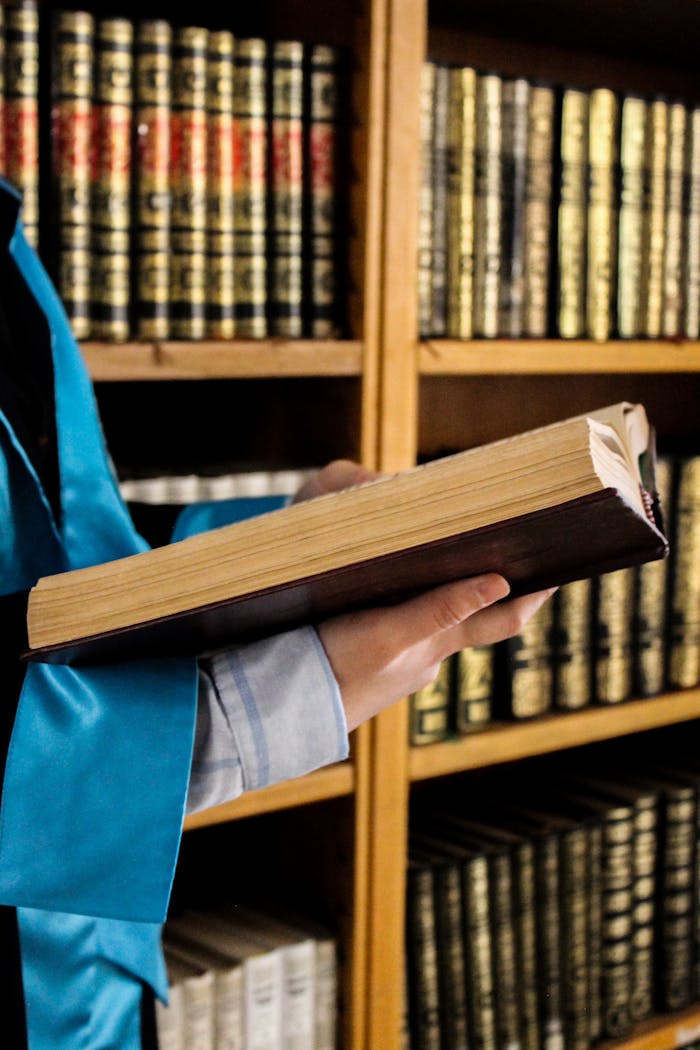 services-02 Adult reading a book in a library, shelves filled with gold-lettered volumes.
