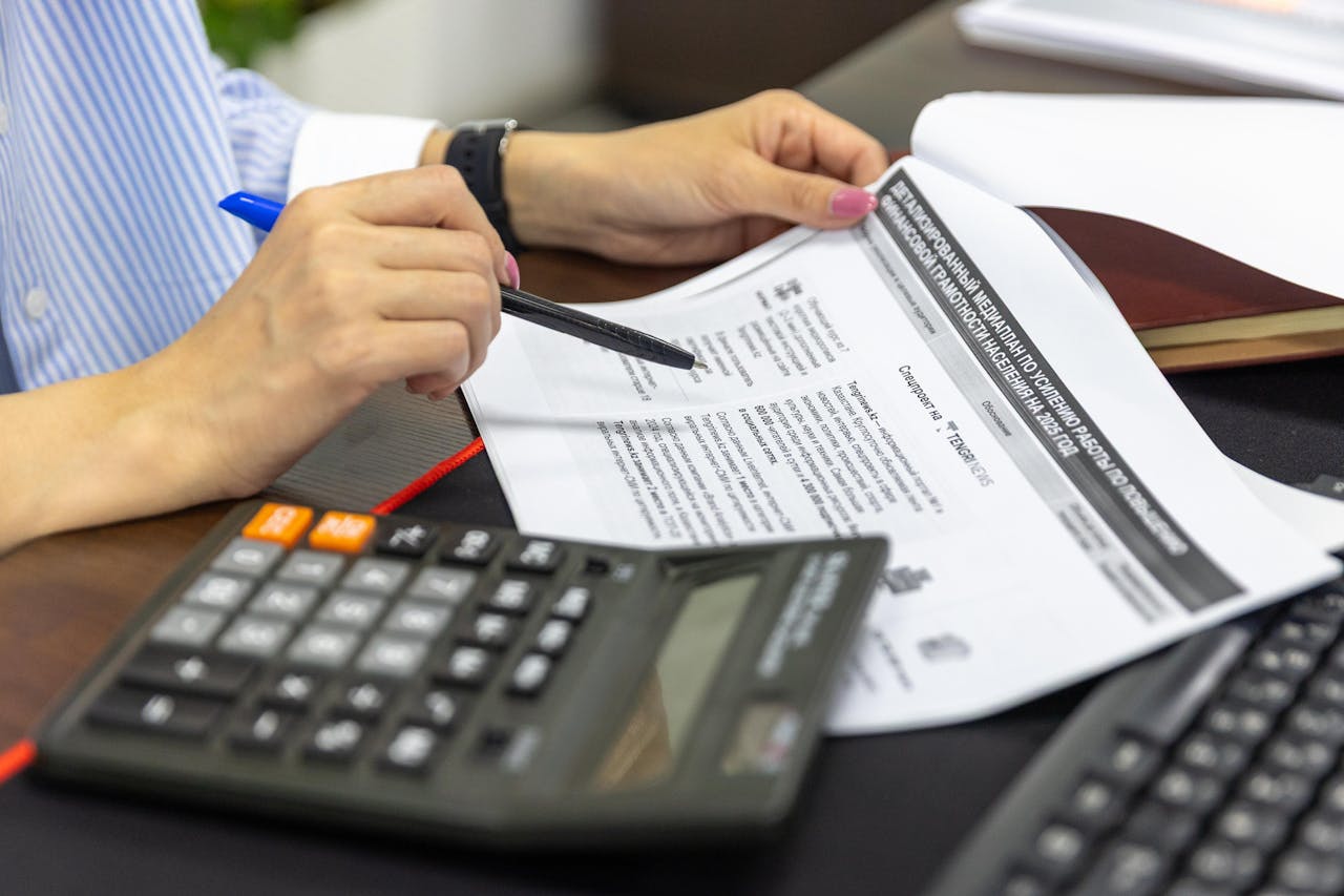 services-01 Close-up of a person analyzing financial documents using a calculator and pen.