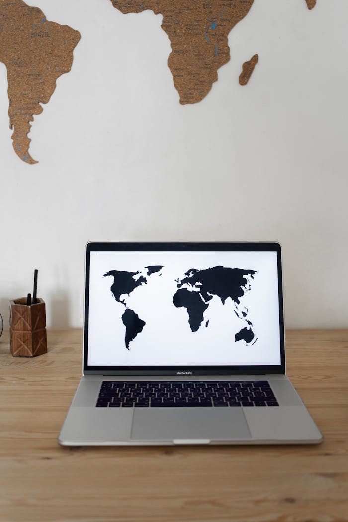 services-03 Laptop with black world map on screen placed on wooden table near white wall with silhouettes of continents
