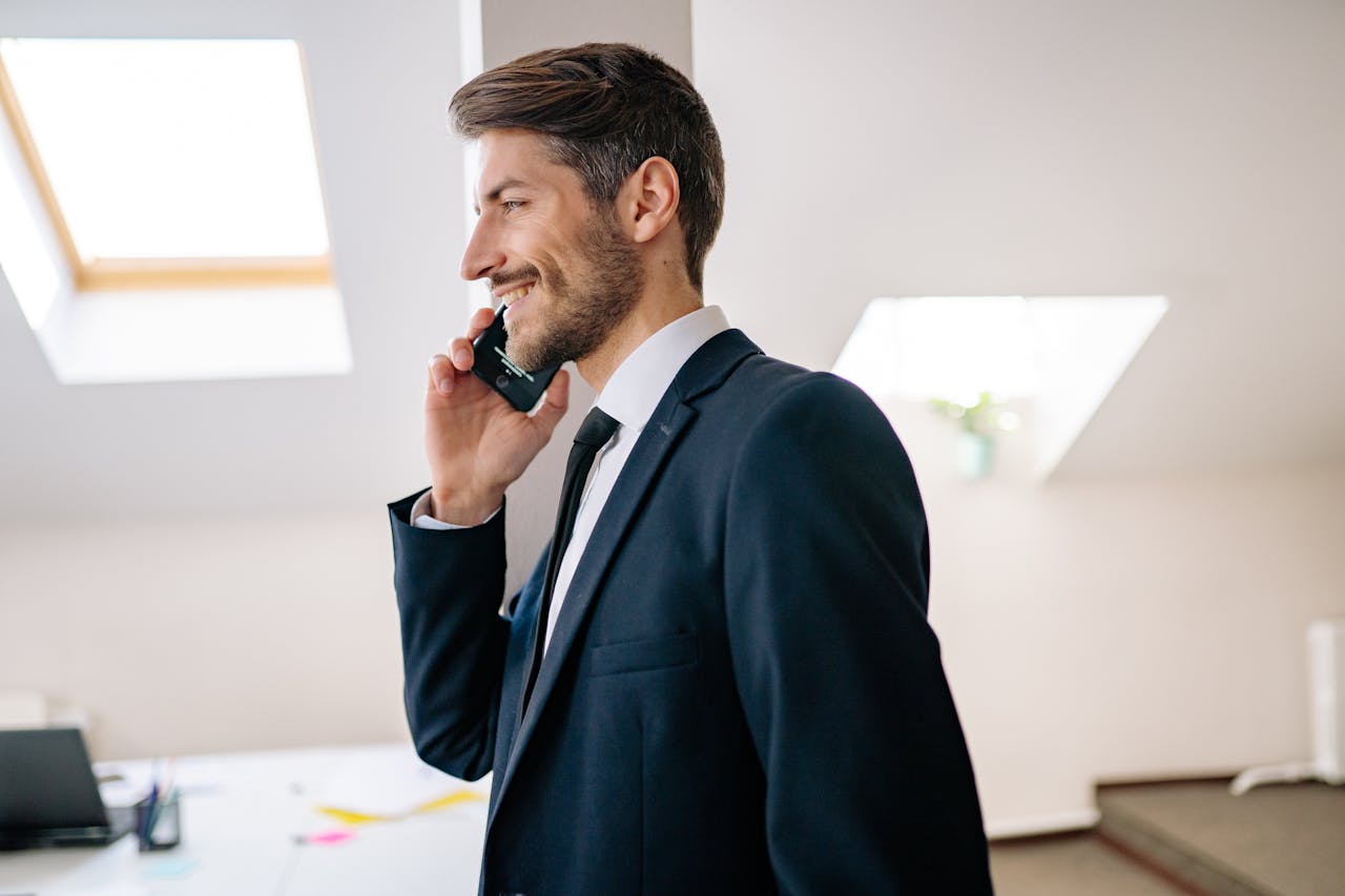 journey Smiling businessman in a suit making a phone call inside a modern office setting.